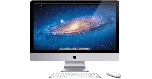 A large flat screen monitor on a stand with a picture of our galaxy on screen. There is a white keyboard and mouse in front.